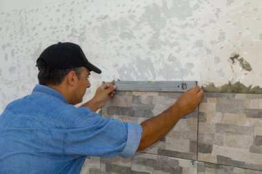 Fayansların doğru yerleştirildiğinden emin olmak için ruh seviyesini kullanan bir klasörün resmi. Kendin-yap restorasyon işi.