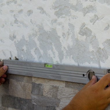 Yeni monte edilen fayansların doğruluğunu bir seviye ile kontrol ederken bir klasörün ellerinin görüntüsü. DIY işleri