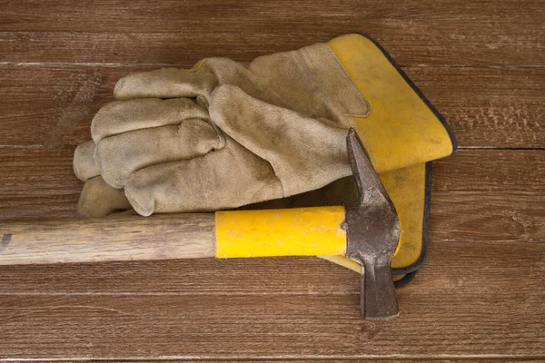 Image of a mason\'s hammer and a pair of work gloves. Reference to manual work and safety at work.
