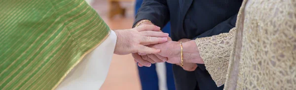 Image of the hands of an elderly couple celebrating 50 years of marriage while the parish priest gives them the blessing. Horizontal banner