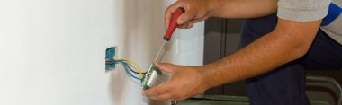 Tamirci bir elektrikçinin ev elektrik prizini tamir edip monte edişinin resmi. DIY güç dolgusu çalışıyor. Yatay Pankart 