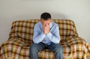 Evdeki kanepede oturan ve baş ağrısı çeken bir adamın görüntüsü. Migreni olan insanlar.