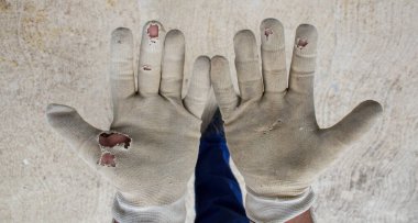 Eldivenleri yırtılmış bir inşaat işçisinin elleri. Yorucu işe referans