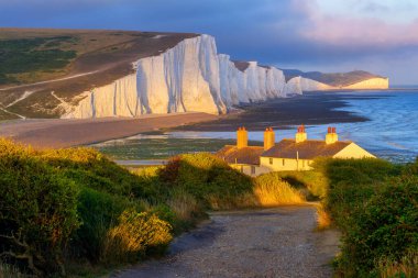 İngiliz Kanalı, Sussex, İngiltere ve İngiltere 'deki Seven Sisters uçurumları gün batımında tebeşirlenir. Beyaz kayalıklar, İngiliz deniz kıyısının önemli bir simgesi ve popüler bir turizm beldesidir..