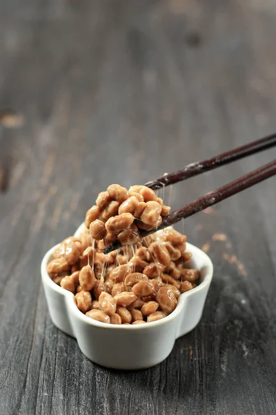 Natto Lifted with Chopstick. Natto is Japanese Fermented Sticky Soy Beans with Stinky Smell. On Wooden Table