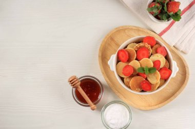 Bowl with Tiny Pancake Cereal with Strawberries and Mint Leaves on a WhiteBackground. and Wooden Plate. Trendy food. Mini cereal pancakes. Landscape Orientation, Copy Space