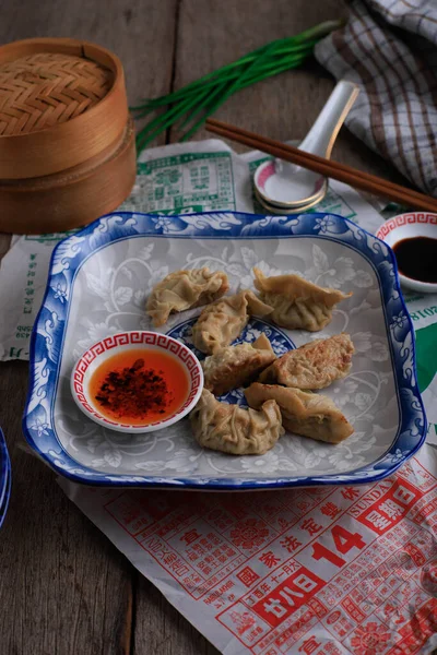 English Translation : Gyoza, Steamed and Grilled Dumpling Stuffed with Cabbage, Serve on CHinese Blue Plate with Chilli Oil