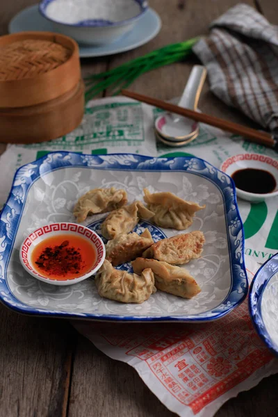 English Translation : Gyoza, Steamed and Grilled Dumpling Stuffed with Cabbage, Serve on CHinese Blue Plate with Chilli Oil