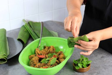Indonesian Woman Wrapped Yellow Curry Chicken with Banan Leaf, Cooking Process Making Pepes Ayam. Tight Banana Leaf with Stick