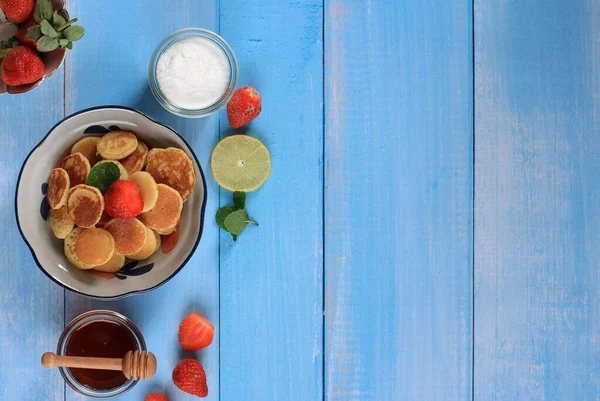 Bowl with Tiny Pancake Cereal with Strawberries, Lemon, and Mint Leaves on a Blue Background. Trendy food. Mini cereal pancakes. Landscape Orientation