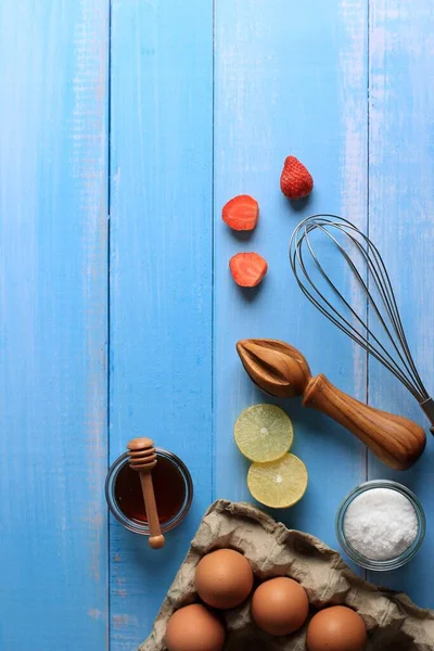 Selective Focus Baking Background with Baking Ingredients such as Egg, Strawberry, Lemon, Sugar Dus, and Honey. Suitable for Background or Wallpaper on Wooden Blue Background