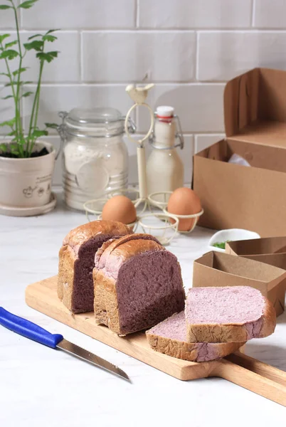 Homemade Purple Bread Made from Japanese Purple Sweet Potato. with natural Color. Served on Wooden Cutting Board White Background with Milk and Brown Paper Package. Concept for Healthy Diet Bakery