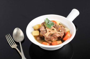 Indonesian Oxtail Soup or Sop Buntut on White Ceramic Plate, Isolated Black Background