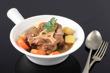 Indonesian Oxtail Soup or Sop Buntut on White Bowl.  Sup Buntut Made from Oxtail Beef with Carrot, Potato, and other Spice, Aromatic and Delicious. Isolated on Black Background