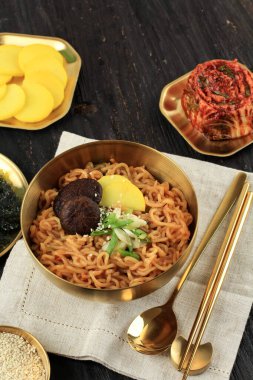 Spicy Fried Ramyeon Korean Instant Noodle with Danmuji, Mushroom, Sesame Seed, Kimchi, and Green Onion. On Wooden Table 