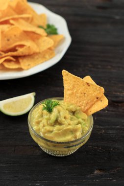 Bowl with Guacamole Dip  and Nachos Tortilla Chips on Wooden Table 