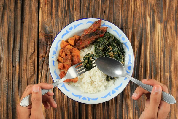 手拿着勺子和叉子吃Nasi Warteg菜单 用Kentang Balado Tongkol Pedas和Stir Fry Papaya叶蒸煮白饭 印度尼西亚迪什 — 图库照片