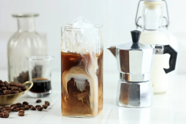 Glass of Homemade Cold Brew Coffee with Milk and Coffee Beans on White Table
