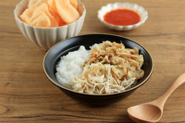 Bubur Ayam or Indonesian Rice Porridge with Shredded Chicken. Served with Kerukpuk (Cracker), Soy Sauce, Fried Soy Bean, and Sambal