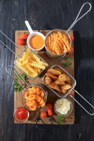 Assorted French Fries and Chips in Metal Baskets on Wooden Table