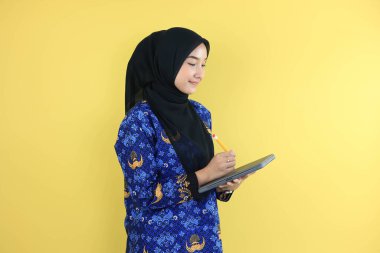 Korpri Batik üniformalı genç bir hükümet çalışanı elinde kalem, evrakları kontrol ediyor. Sarı Arkaplanda İzole Edildi