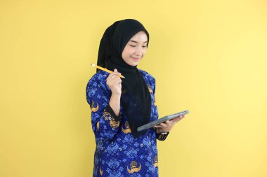 Korpri Batik üniformalı genç bir hükümet çalışanı elinde kalem, evrakları kontrol ediyor. Sarı Arkaplanda İzole Edildi