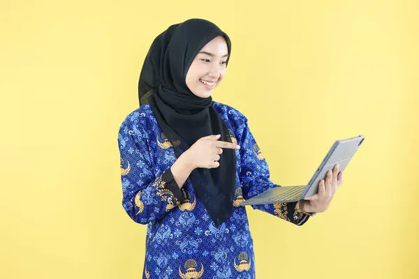 stock image Cheerful Muslim Government Worker or ASN  Woman in Blue Korpri Batik Uniform pointing at Laptop, Happy Face Expression