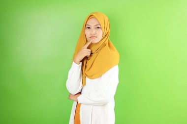 Asyalı genç tesettürlü kadın somurtuyor ve düşünüyor, kameraya bakıyor, üzgün jest yapıyor. Yeşil Arkaplanda ISolated 