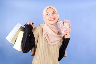 Peçeli Asyalı Müslüman Kadın Nakit Rupiah Para ve Kağıt Torba, Alışveriş Konsepti. Mavi Arkaplanda İzole Edildi