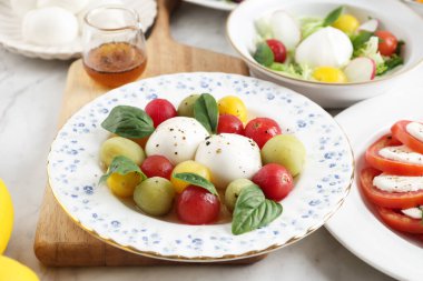 Sarı, Yeşil ve Kırmızı Domates Kirazlı Salata ve Beyaz Tabakta Mozzarella Peyniri. Bocconcini Mozza Peynirli Taze Casil Yaprakları Caprese Salatasında.