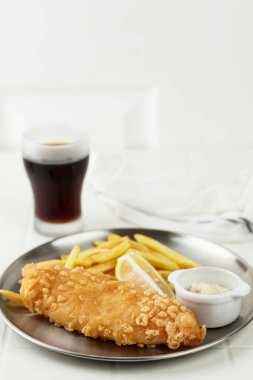 Fish and Chips, un hamurunda kızarmış balık, patates kızartması ve kola ile servis edilir. Metalik Tabaka