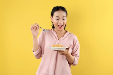 Mutlu Cazibeler, Çekici Asyalı Genç Kadın, Çatal Yeme Anında Erişte veya Mie Goreng Beyaz Tabakta, Sarı Arkaplanda Metin İçin Boşluğu Kopyala 