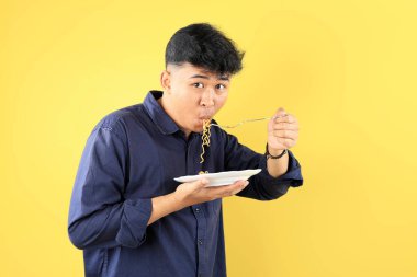 Endonezyalı Genç Öğrenci Paslanmaz Çatal kullanarak anında erişte yiyor. Sarı Arkaplanda 