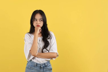 Asyalı genç kız somurtuyor. Ağzı bozuk ve mutsuz. Boşluğu Sarı Arkaplanda Kopyala 