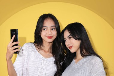 İki Nesil Z Selfie Çekiyor, Genç Asyalı Bestie Kız Cep Telefonu ile Fotoğraf Çekiyor. Sarı Arkaplanda İzole Edildi 