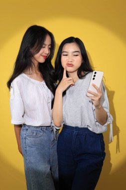 İki Nesil Z Kızı Selfie Çekiyor, Genç Asyalı Bestie Kız Cep Telefonu ile Fotoğraf Çekiyor. Sarı Arkaplanda İzole Edildi