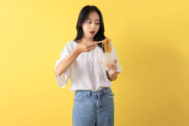 Genç Endonezyalı Harika Pop Mie Noodle Cuup, Chopstick kullanarak Anında Erişte yiyin. Sarı Arkaplanda İzole Edildi 