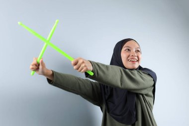 Yeşil Çubukla Pound Fit antrenmanı yapan bir Hijabi Kadını, Gri Arkaplanda tecrit edilmiş. Kapat, Düşük Açı