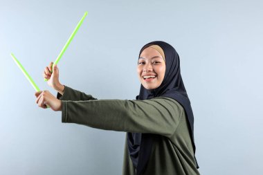 Yeşil Çubukla Pound Fit antrenmanı yapan bir Hijabi Kadını, Gri arka planda izole edilmiş.