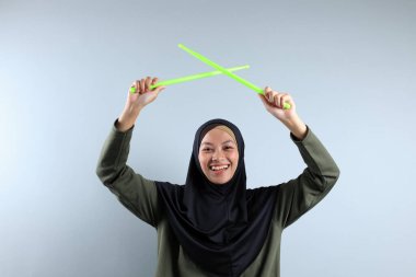 Yeşil Çubukla Pound Fit antrenmanı yapan bir Hijabi Kadını, Gri arka planda izole edilmiş.