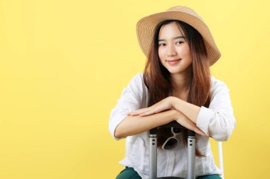 Mutlu gülümseyen Asyalı kadın turist yaz şapkalı ve çantalı güneş gözlüklü, sarı arka planda izole edilmiş 