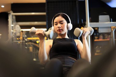 Spor salonunda müzik dinlerken dambılları kullanan genç bayan eğitimi. 