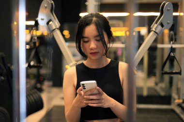 Spor salonundaki spor salonunda cep telefonuyla oturan genç bir bayan. 