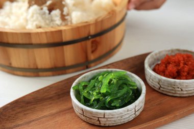 Susam tohumlu Wakame Seaweed Salatası ve tahta tabakta küçük bir kâse içinde acı biber.