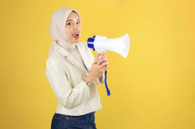 Cream Blazer ve Jeans 'li Mutlu Müslüman Genç Asyalı Kadın Sarı Arkaplanda Megafonla Haber ya da İndirim Satışı Yapıyor 