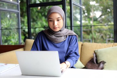 Kafe 'de İnternet' te çalışan Asyalı Müslüman Kadın Laptop ve Kahve ve Çay 'ı kullanıyor. Front View Endonezyalı Serbest Çalışan Kadın Dizüstü bilgisayarda Yazıyor, İşini Her Yerde Zevkle Yapıyor