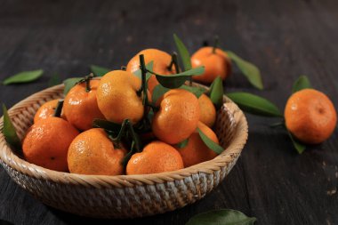 Taze olgun Sicilya Mandalinalarını, Tahta Masa 'daki Rattan Bowl' da Yeşil Yapraklarla Kapatın