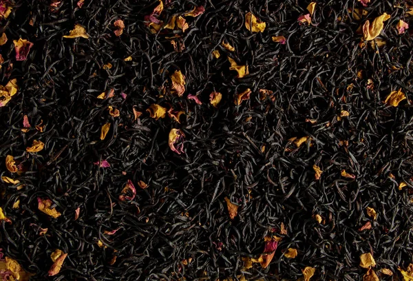 A mixture of dry black tea and dry tea rose petals as a background.