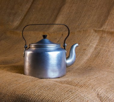 An old soldier's aluminum teapot from the Second World War against the background of burlap.