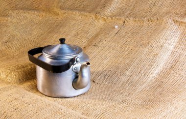 An old soldier's aluminum teapot from the Second World War against the background of burlap.